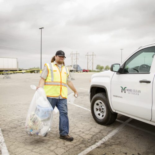 More Clean of Texas employee in high visibility vest carrying a bag of trash to company truck